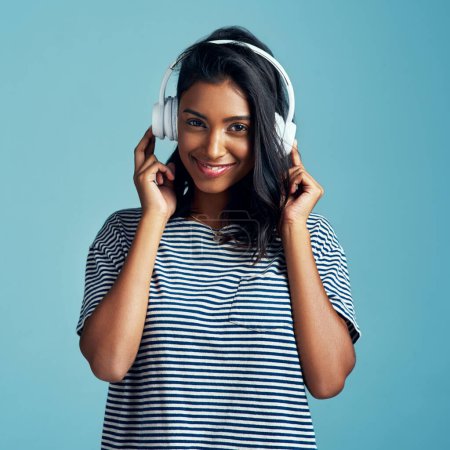 Photo for Woman, portrait and headphones with music in studio with happiness and web audio. Blue background, Indian female person and young model listening, hearing and streaming a song with smile and online. - Royalty Free Image