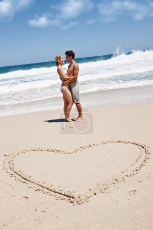 Foto de Cada verano tiene una historia. una joven pareja disfrutando de un momento romántico en la playa junto a un dibujo de un corazón en la arena - Imagen libre de derechos