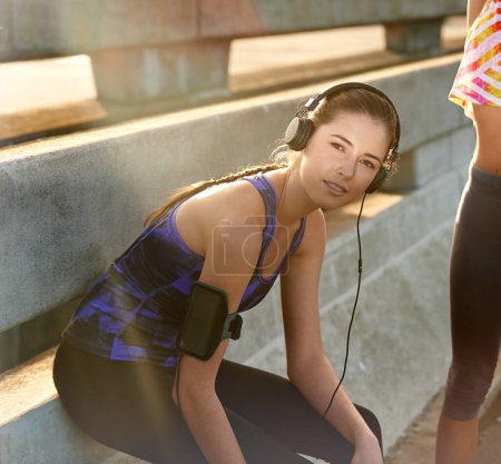 Téléchargez les photos : J'écoute ma bande son. Portrait d'une jeune joggeuse écoutant de la musique avant une course avec un ami à travers la ville - en image libre de droit