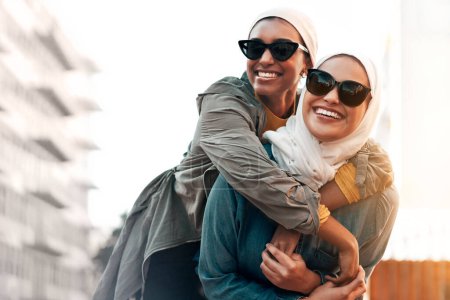 Téléchargez les photos : Femme musulmane, amis et piggyback dans la ville avec la liberté, la jeunesse et les voyages urbains ensemble au Qatar. Femmes islamiques, bonheur et marche dans le métro avec jeu drôle, lunettes de soleil et voyage comique. - en image libre de droit