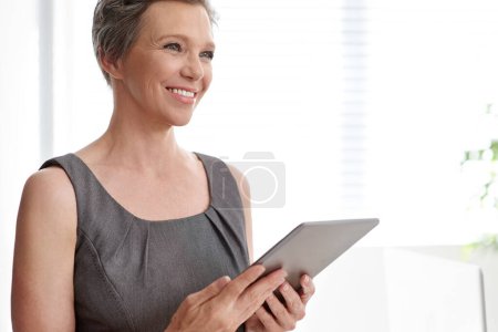 Téléchargez les photos : Utiliser la technologie à son avantage. Une femme d'affaires mature regardant réfléchi tout en tenant sa tablette numérique - en image libre de droit