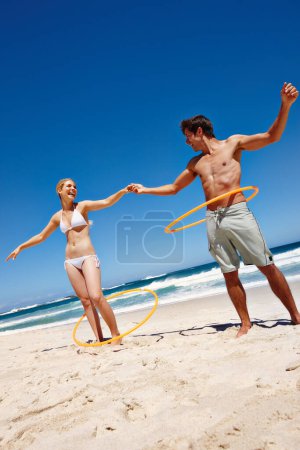 Foto de Gira en nombre del amor. una feliz pareja joven bailando con aros de plástico en la playa - Imagen libre de derechos