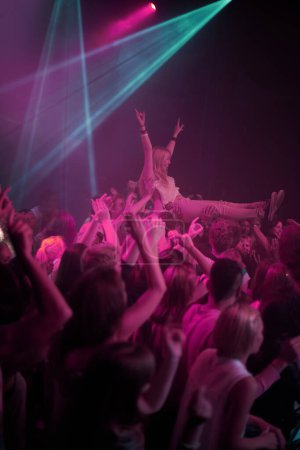 Foto de Surf multitudinario, neón y gente en el festival de música con iluminación rosa neón y energía en el evento de concierto en vivo. Baile, diversión y grupo de fans emocionados de gen z en la arena en la actuación de la banda de rock o fiesta de la audiencia - Imagen libre de derechos