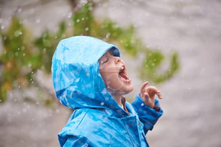 Photo for Winter, raincoat and a girl having fun in the rain outdoor alone, playing during the cold season. Kids, water or wet weather with an adorable little female child standing arms outstretched outside. - Royalty Free Image