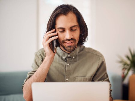 Foto de Manejando llamadas de negocios. un joven hombre de negocios hablando por celular mientras usa un portátil en una oficina - Imagen libre de derechos