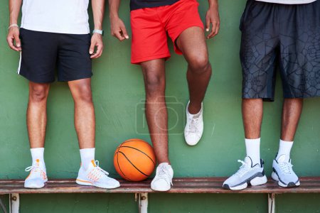 Téléchargez les photos : Défendez les champions. Gros plan d'un groupe d'hommes sportifs debout sur un banc à côté d'un ballon de basket contre un mur - en image libre de droit