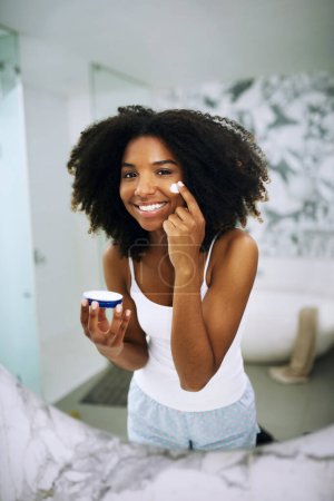 Photo for Skincare, smile and portrait of black woman in bathroom mirror with cream, dermatology and morning routine. Health, wellness and luxury skin care at home, happy girl in reflection with lotion on face. - Royalty Free Image