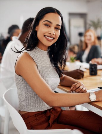 Photo for Im always positive about what we can achieve together. Portrait of a young businesswoman sitting in an office with her colleagues in the background - Royalty Free Image