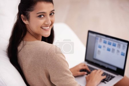 Photo for Shes an internet addict. A young woman sitting on her sofa working on her laptop - Royalty Free Image