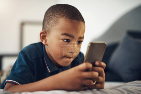Foto de Este rompecabezas es un poco complicado. un niño usando un celular mientras está acostado en su cama - Imagen libre de derechos