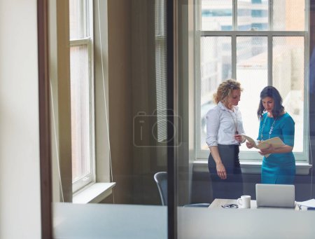 Foto de Compartiendo una actualización con su colega. dos empresarias revisando el papeleo juntas en una oficina - Imagen libre de derechos
