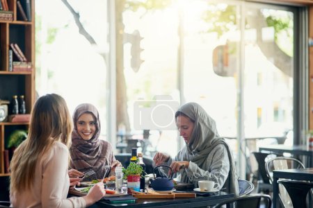 Téléchargez les photos : Amis, femmes heureuses et musulmanes au restaurant, mangeant et parlant ensemble. Déjeuner, sourire et filles islamiques, discussion de groupe ou de personnes, conversation et discussion pour une réunion sociale, des liens et de la nourriture - en image libre de droit
