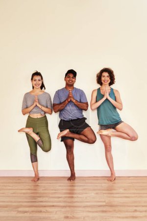 Foto de Mantén tus raíces profundas y tus ramas altas. un grupo de hombres y mujeres jóvenes que practican la pose del árbol durante una sesión de yoga - Imagen libre de derechos