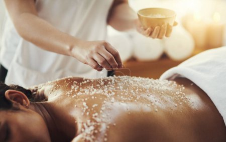 Mujer, manos y sal en masaje en spa para cuidado de la piel, exfoliación o tratamiento corporal en resort. Mano de masajista aplicando sales a la espalda de la piel para la relajación, terapia o zen en el bienestar saludable en el salón.