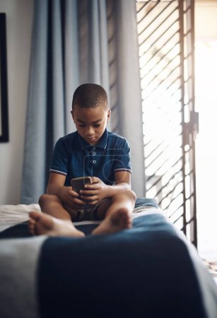 Foto de Aprender nuevas palabras en línea. un niño usando un celular mientras está sentado en su cama - Imagen libre de derechos