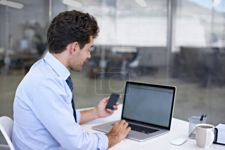 Foto de Buscando el número de contacto de un cliente. Un joven empresario sentado en su escritorio con un teléfono móvil en la mano - Imagen libre de derechos