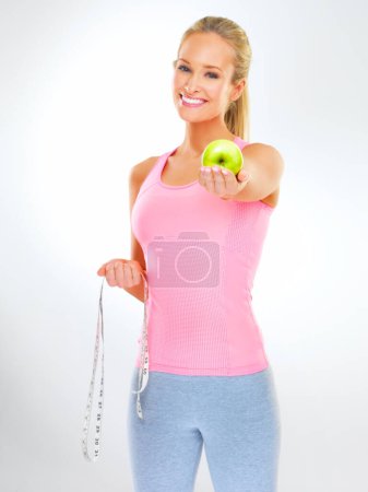 Téléchargez les photos : Prenez une bouchée de régime. Plan studio d'une jeune femme avec une pomme et un ruban à mesurer - en image libre de droit