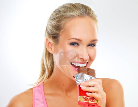 Téléchargez les photos : Tout avec modération. forme jeune femme en vêtements d'exercice manger une barre de chocolat - en image libre de droit