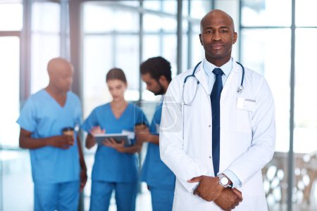 Photo for Your health is my first point of concern. Portrait of a mature doctor standing in a hospital with his colleagues in the background - Royalty Free Image