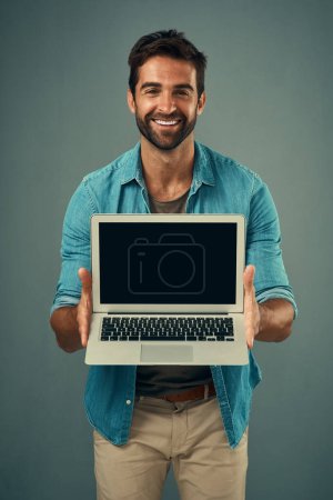 Foto de Tengo algo emocionante que mostrarte. Retrato de estudio de un joven guapo sosteniendo un portátil con una pantalla en blanco sobre un fondo gris - Imagen libre de derechos