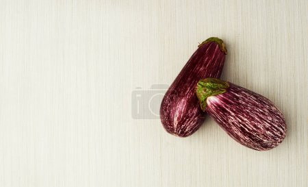 Photo for Enticing eggplants. Top view of two aubergines lying on a light wooden surface - Royalty Free Image