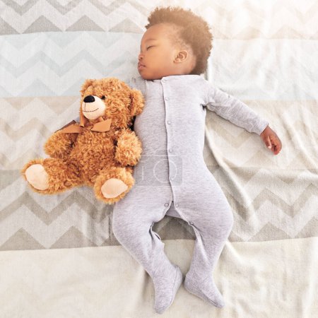 Photo for Top view, teddy bear and baby sleeping in bed for rest, nap time and dreaming in nursery. Childcare, newborn and cute, tired and African child with toy in bedroom sleep for comfort, relax and calm. - Royalty Free Image