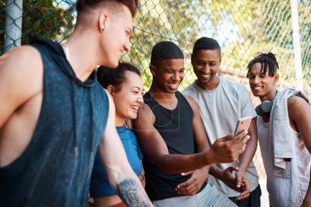 Photo for Told you this would be hilarious. a group of sporty young people looking at something on a cellphone while standing along a fence outdoors - Royalty Free Image