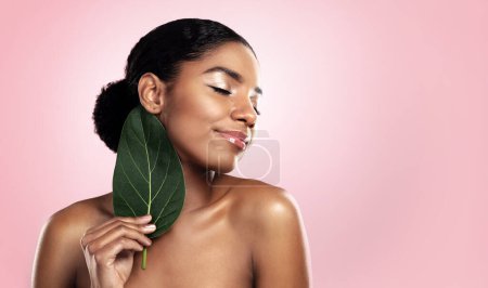 Photo for Happy woman, leaf and natural beauty in studio, pink background and mockup for aesthetic cosmetics. Face, african model and skincare from plants, green leaves and sustainability of vegan dermatology. - Royalty Free Image