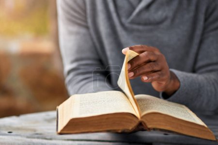 Hands, spiritual and a man reading the bible at a table outdoor in the park for faith or belief in god. Book, story and religion with a male christian sitting in the garden for learning or worship.