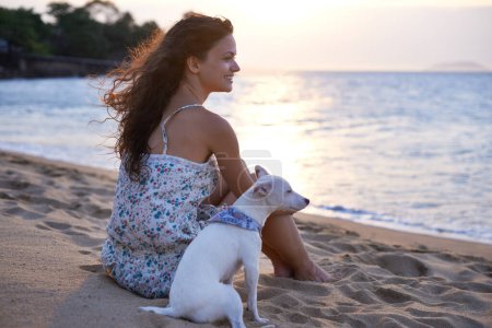Foto de Observando la puesta de sol en la playa. una joven atractiva disfrutando de la playa con su perro - Imagen libre de derechos