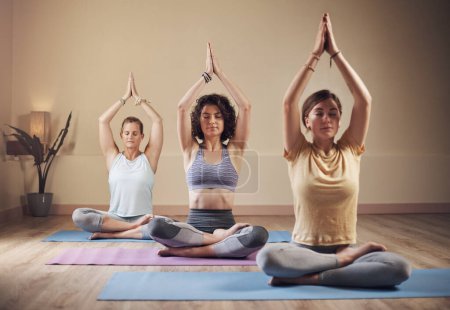 Foto de El yoga es energía. Largometraje de un grupo joven de mujeres sentadas juntas y meditando después de una sesión de yoga en interiores - Imagen libre de derechos