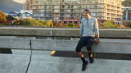 Téléchargez les photos : Prendre l'aube sur une course du matin. un jeune joggeur assis sur le bord de la route tout en prenant une pause d'une course - en image libre de droit