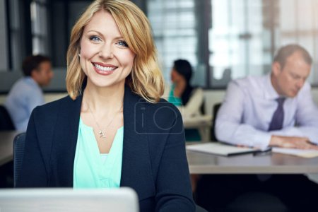 Foto de La positividad aumenta mi productividad. Retrato de una mujer de negocios usando un portátil en su escritorio con sus colegas en el fondo - Imagen libre de derechos