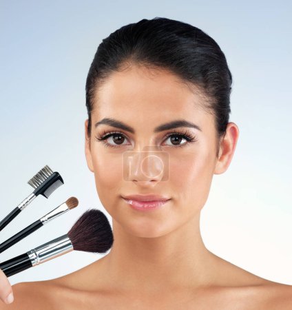 Photo for The tools I use to look my best. Studio shot of a beautiful young woman holding makeup brushes against a gray background - Royalty Free Image