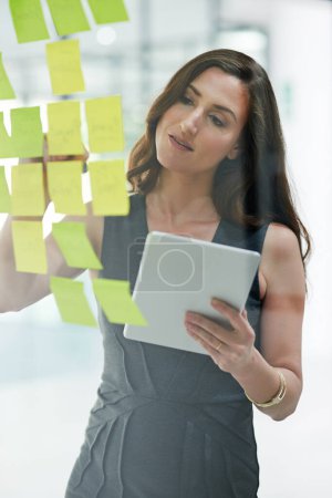 Photo for Tablet, glass wall and business woman writing, planning and strategy in office workplace. Sticky notes, brainstorming and female professional with technology for working on ideas, schedule and info - Royalty Free Image
