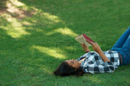Foto de Relajarse con un buen libro. una joven acostada en la hierba y leyendo un libro - Imagen libre de derechos