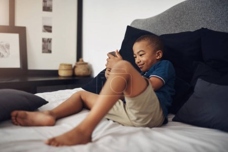 Foto de Estoy emocionado por un poco de diversión en línea. un niño usando un celular mientras está sentado en su cama - Imagen libre de derechos