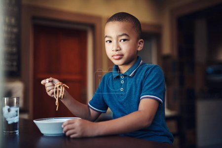 Téléchargez les photos : Je suis un mangeur difficile, mais pas quand il s'agit de spaghettis. un jeune garçon mangeant un bol de spaghettis à la maison - en image libre de droit