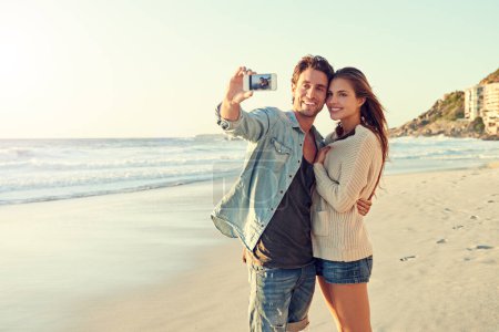 Téléchargez les photos : Capturer de beaux moments estivaux. un jeune couple aimant prendre un selfie à la plage - en image libre de droit