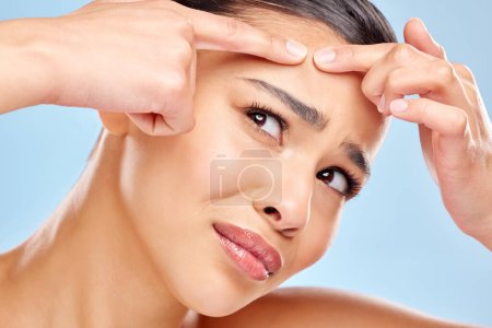 Photo for Dear pimple, why are you here. Studio shot of an attractive young woman squeezing a zit on her face against a blue background - Royalty Free Image