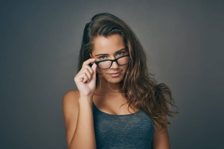 Foto de Usando el doble de ojos. Foto de estudio de una atractiva joven mirando sus gafas sobre un fondo gris - Imagen libre de derechos