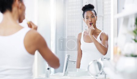 Téléchargez les photos : Femme brossant les dents dans la salle de bain, miroir avec hygiène dentaire et buccodentaire avec routine matinale, brosse à dents et santé. Femme à la maison, toilettage et autosoin avec bouche propre et bien-être. - en image libre de droit