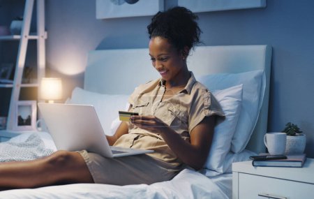 Téléchargez les photos : Carte de crédit, femme et nuit dans un lit avec des achats en ligne et le bonheur de l'achat. Chambre à coucher, boutique en ligne et e-commerce affaire d'une femme africaine dans une maison en essayant de payer sur une application web. - en image libre de droit