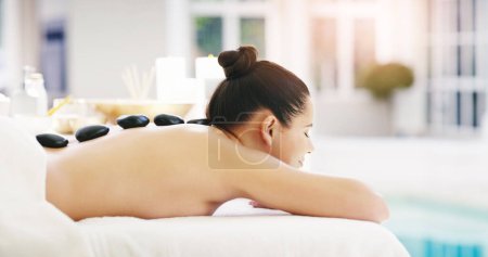 Foto de Mujer, relax y masaje de roca en el spa para zen, fisioterapia o tratamiento en el resort. Persona femenina feliz que relaja con la piedra caliente detrás para el alivio del músculo, tensión o bienestar pacífico en un salón. - Imagen libre de derechos
