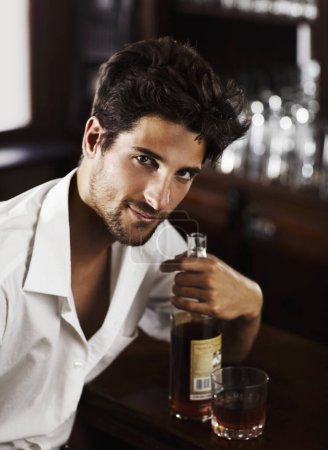 Photo for Man, pub counter and portrait with drink at happy hour with alcohol and whiskey after work. Bottle, male person and face of a handsome guy with a glass and style and confidence in a luxury bar. - Royalty Free Image