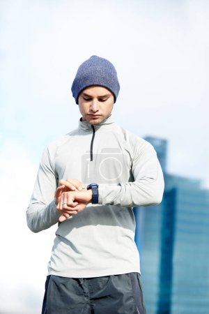 Téléchargez les photos : Temps écoulé. un jeune joggeur vérifiant l'heure tout en dehors pour une course dans la ville - en image libre de droit