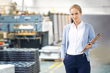 She has this factory running smoothly. Portrait of a smiling young manager holding a clipboard while standing on the factory floor