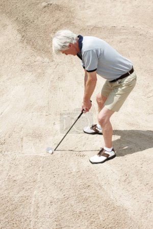 Téléchargez les photos : Coincé dans le piège à sable. Senior homme essayant de frapper sa balle hors du piège à sable sur le terrain de golf - en image libre de droit