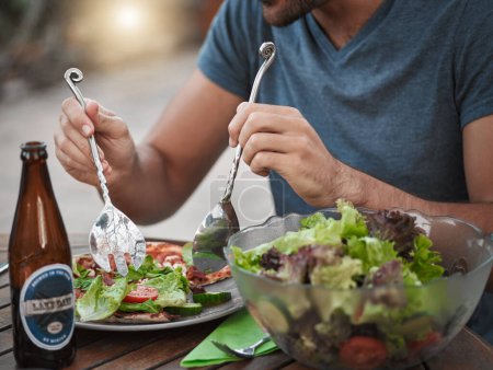 Téléchargez les photos : Jeter la salade. un homme méconnaissable qui se prépare de la salade dans une assiette tout en étant assis dehors autour d'une table - en image libre de droit