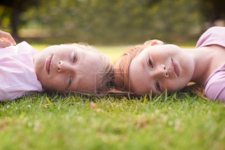 Téléchargez les photos : Des moments d'enfance. Deux petites filles allongées joyeusement sur l'herbe et riant - en image libre de droit